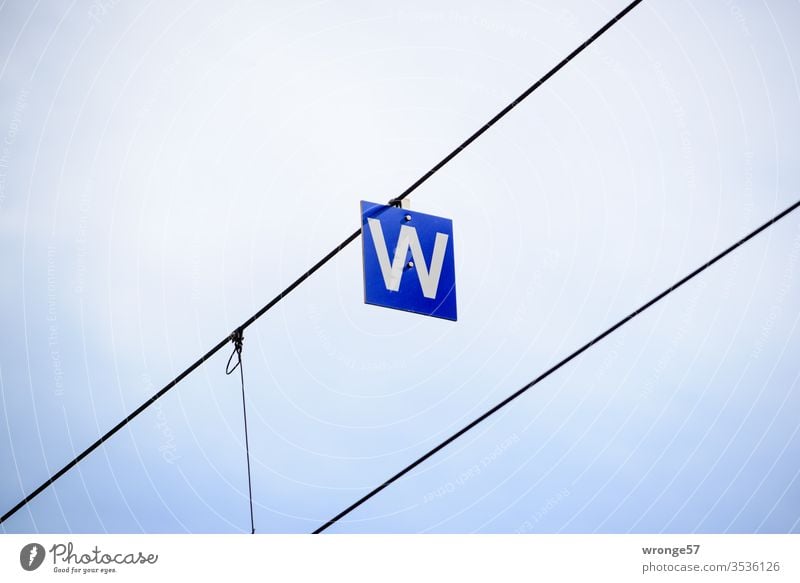 A white W on a blue board hanging from a wire letter White Blackboard sign Signs and labeling Exterior shot Deserted Colour photo Characters Letters (alphabet)