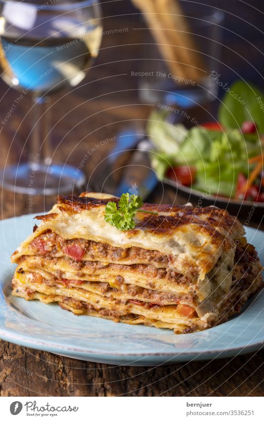Portion of fresh lasagne on a plate Lasagne Evening grissini Summer Vine White wood Rustic Lettuce Meat Minced meat Slice Delicious herbs Bolognese Bolognaise