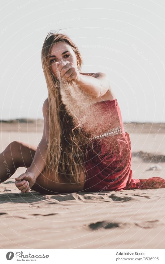 Stylish young lady sitting on beach and pouring sand through fingers woman dream sensual style summer alone coast freedom charming blond attractive beautiful