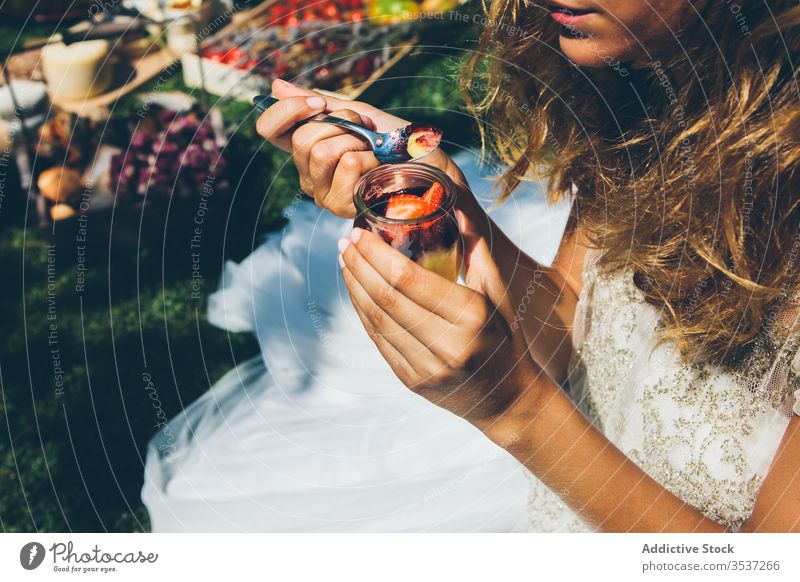 Anonymous young lady in white wedding dress eating berries dessert in garden woman summer fruit celebrate elegant fresh sweet party lunch spoon food strawberry