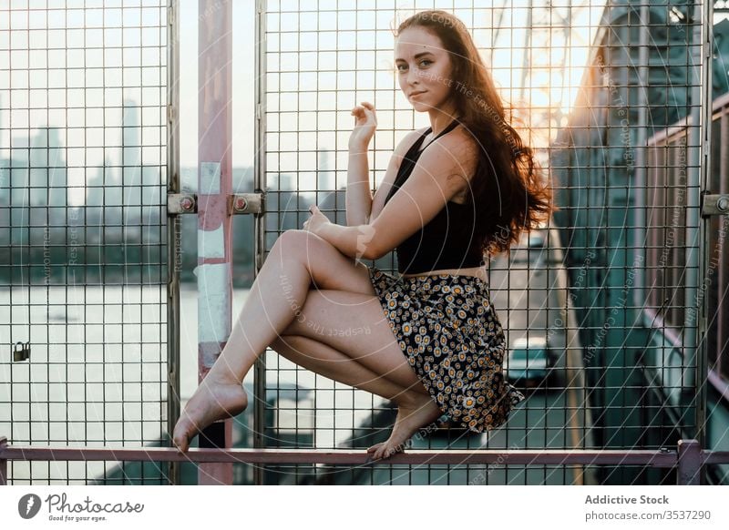 Young female dancer sitting on metal railing of bridge woman grace balance industrial urban cityscape barefoot young tranquil serene calm quiet fence handrail