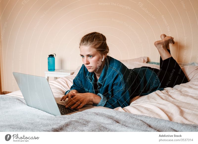 Woman watching movie on laptop in cozy bedroom woman home using lying down surfing social media listen female interest film earphones lounge wireless thoughtful