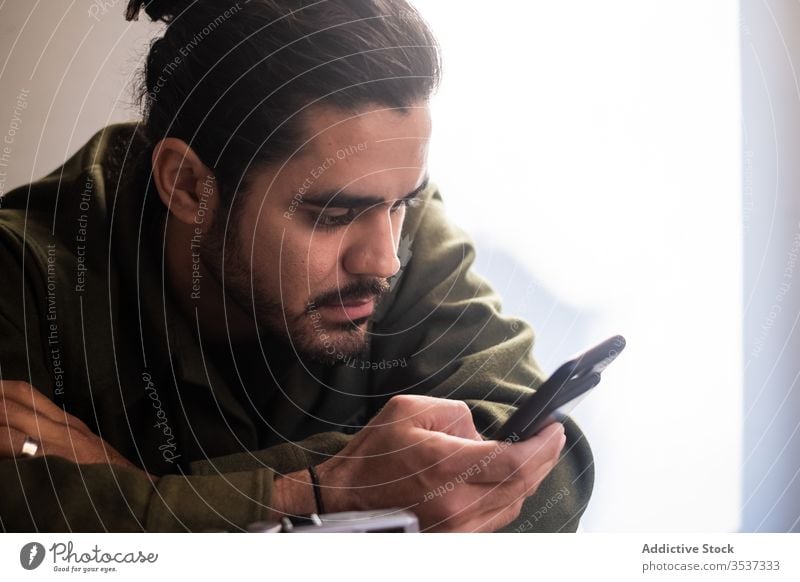 Serious man using smartphone in light room beard browsing surfing pensive handsome message ethnic mobile gadget communicate casual internet connection