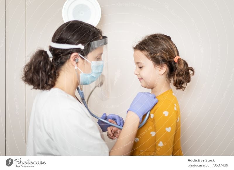 Female doctor examining lungs of little girl in clinic woman mask patient lunge stethoscope hospital glove pneumonia check up covid 19 infection examine virus