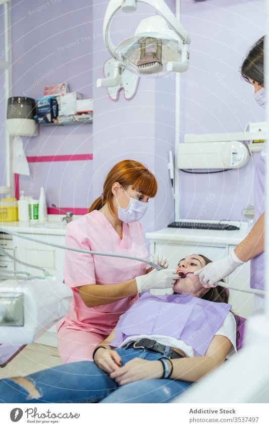 Female dentist with assistant curing patient teeth in clinic women mask dental doctor stomatology uniform medicine treat hospital procedure dentistry equipment