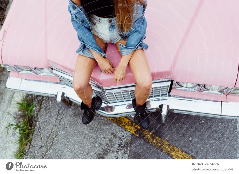 Unrecognizable blonde girl sitting on the hood of a classic pink car on the street woman young braids sidewalk old grunge summer portrait leisure urban city