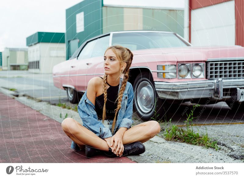 Attractive blonde girl sitting on the sidewalk near to a classic pink car woman young braids old grunge summer portrait leisure urban city outskirts attractive