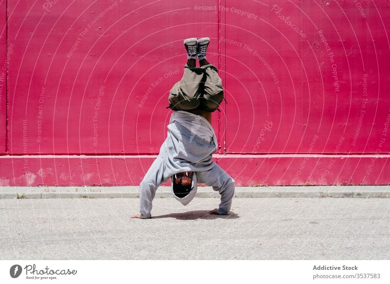 Young hispanic men doing acrobatics near to a pink wall on the street urban dance lifestyle city posing standing colorful daylight mixed hat hip-hop cool modern