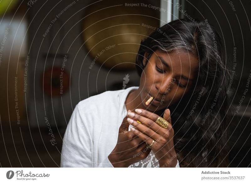 Ethnic woman smoking weed on terrace smoke marijuana relax enjoy roll up young cigarette female ethnic indian hindu casual outfit apparel eyes closed stand dope