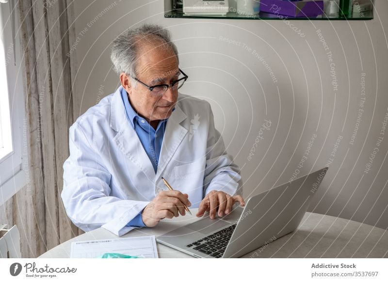 Elderly male physician conducting telemedicine consultation via laptop in clinic man elderly doctor telehealth outbreak using senior aged gray hair medical gown