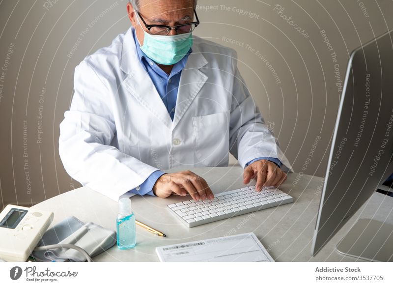 Elderly male physician conducting telemedicine consultation via laptop in clinic man elderly doctor telehealth outbreak using senior aged gray hair medical