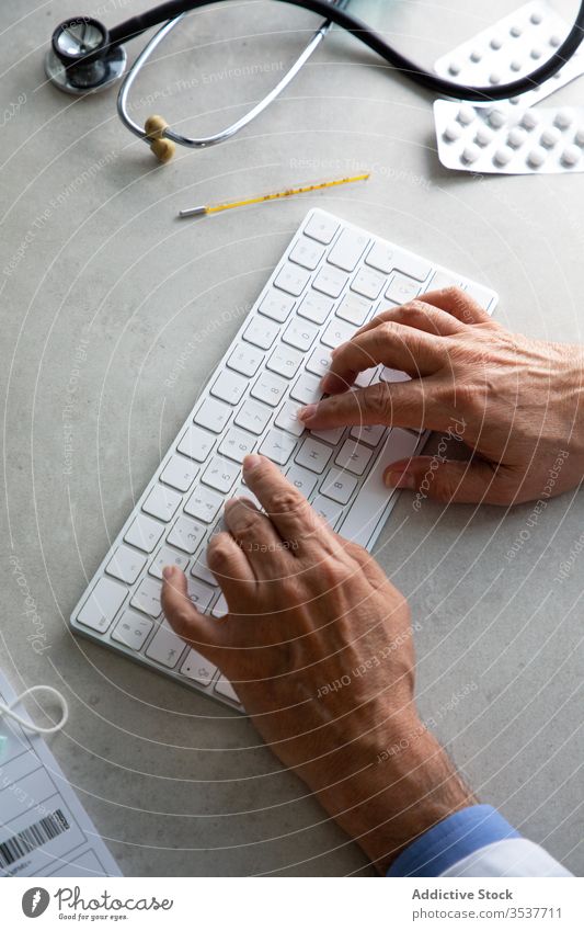 Crop male doctor typing on keyboard during remote work telemedicine man senior prescription internet online consult quarantine coronavirus using elderly
