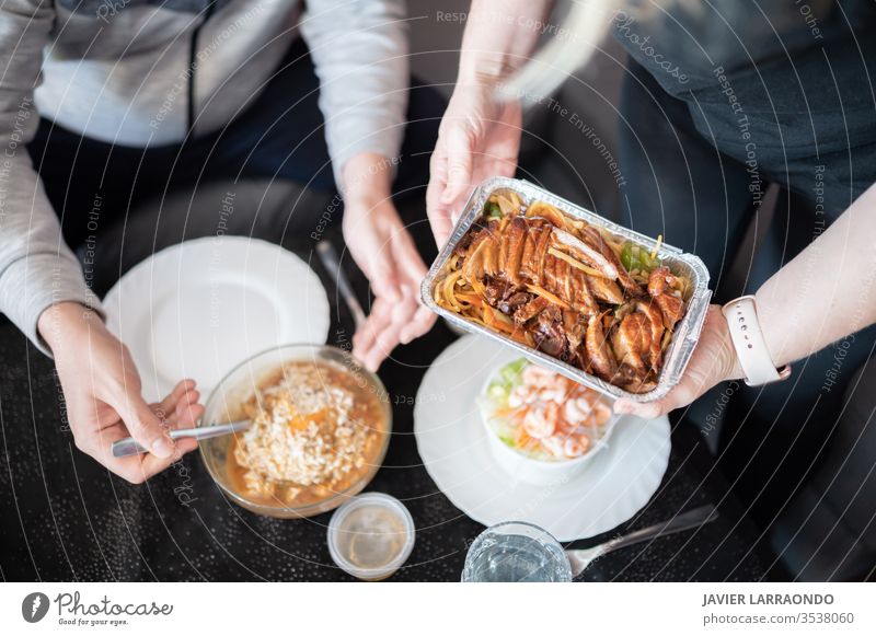 Top view of a woman holding a metal container with Chinese food and her partner ready to eat in unfocused background. Eating at home during isolation by Covid19.Family together