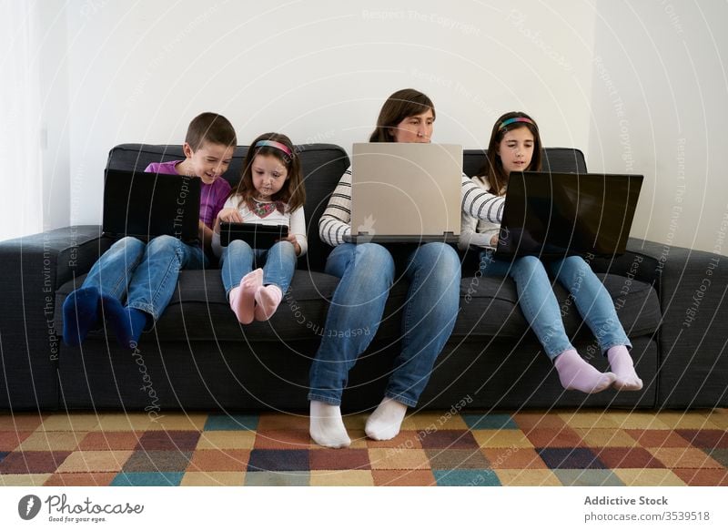 Serious mother and kids spending time together using gadgets on sofa at home children laptop busy addict browsing woman leisure separate sibling parent internet