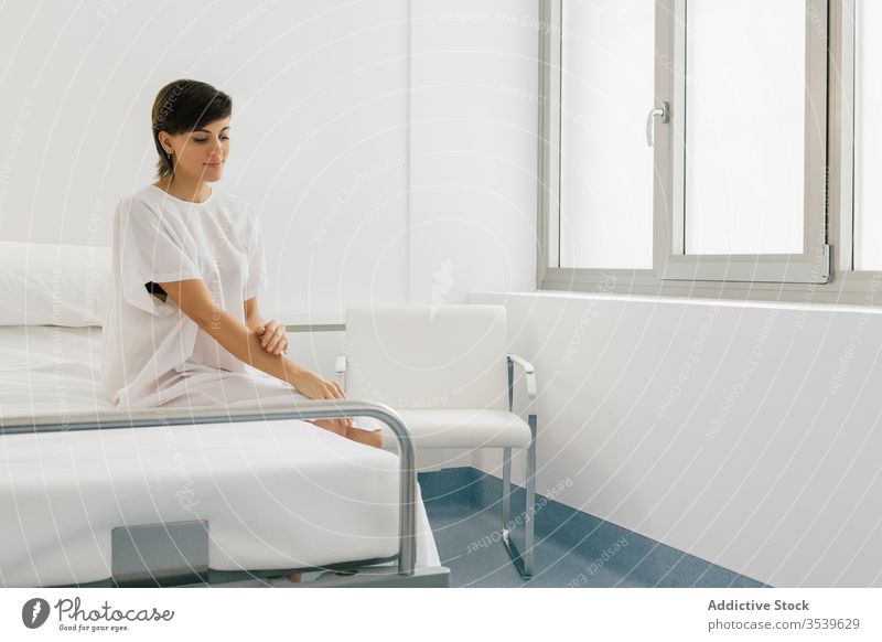 Positive female patient sitting on bed in hospital woman ward positive robe modern light white glad joy clinic happy rest relax room medicine comfort lady
