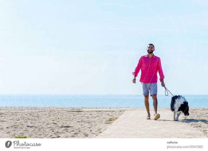 Young bearded man walking with his dog tied up on the beach person pet animal outdoor friendship male sea adult nature summer lifestyle sky happiness sand