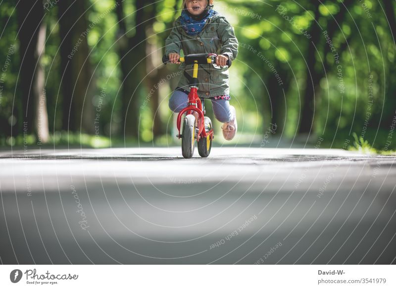 Child rides his bike outside through nature Infancy Joy Bicycle Cycling Small Toddler girl Cute swift children smile Mouth Handlebars To hold on Park Street