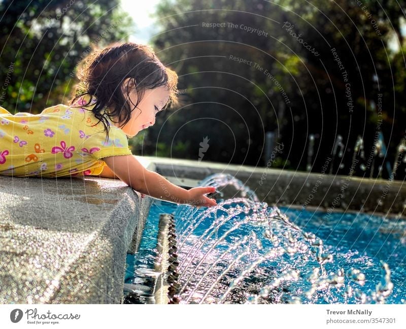 Girl Playing With Water Fountain in Sunshine lifestyle refreshment splashing sunlight toddler little person laughing heat sprinkler grass baby kids funny curly