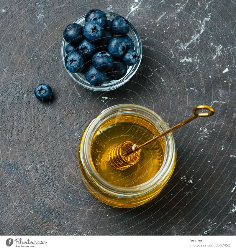 Blueberries and honey on dark background, top view blueberries healthy food ingredients glass jar dipper fresh small bowl over flat lay square crop copy space