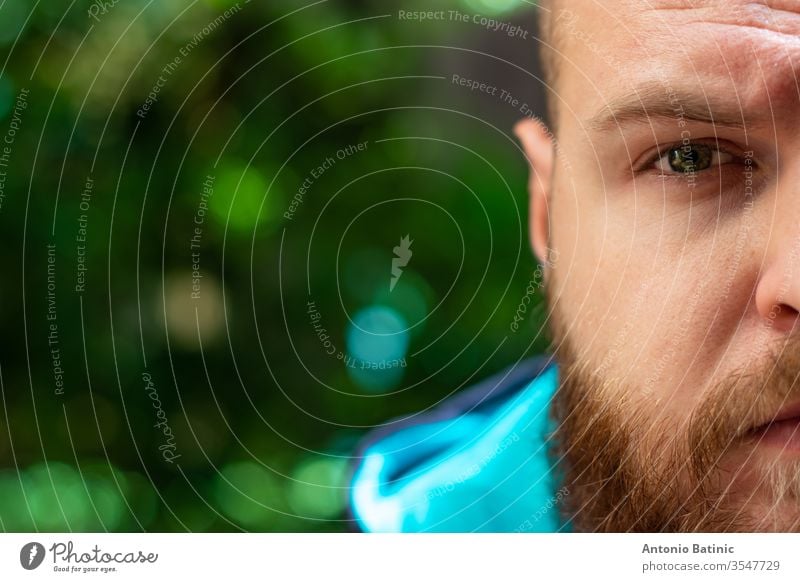 Half head of a bald bearded man visible, green serious sad eye shining in focus on green forest background. adult angry blue brutal casual caucasian confidence
