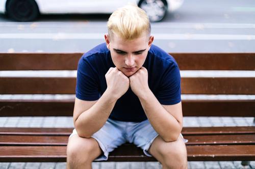 Young boy sitting on a bench in the street with his hands on his face worried and sad man 1 male person young single worry stress park one problem guy sorrowful