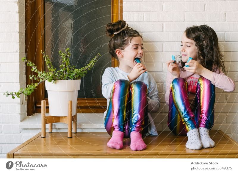Cheerful little girls eating blue chewing candy treat sweet share home fun happy children tasty laugh yummy sister pajama cozy relax childhood playful enjoy