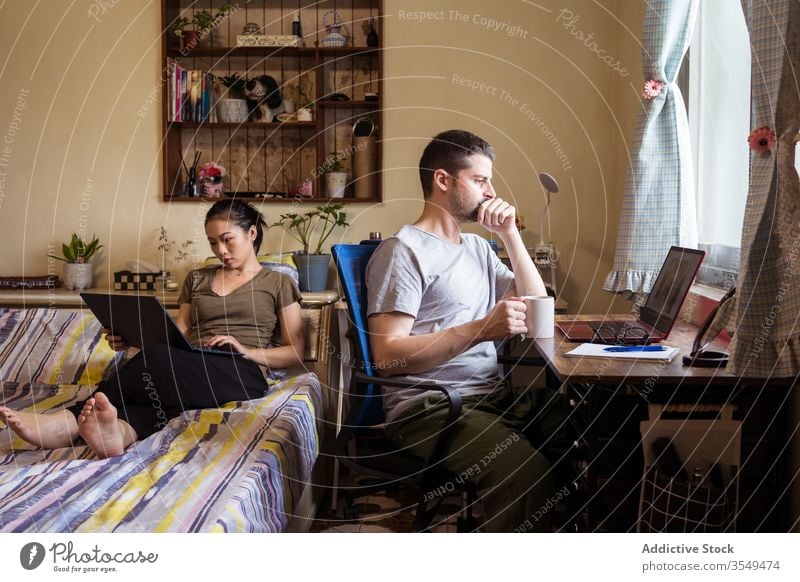 Multiethnic couple of freelancers using laptops at home office work browsing busy entrepreneur multiracial multiethnic diverse asian self employed casual outfit