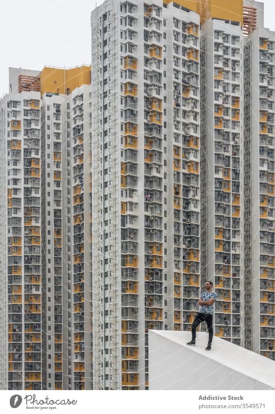 Confident stylish man posing on roof against high rise buildings in Shek Kip Mei Man high-rise multi-storey residential condo dense slope skyscraper district