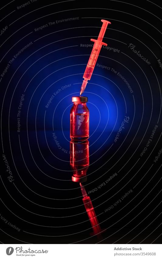 Syringe with needle in dark room in cap of bottle syringe vaccine medication drug cure covid 19 infection virus coronavirus neon illuminate transparent