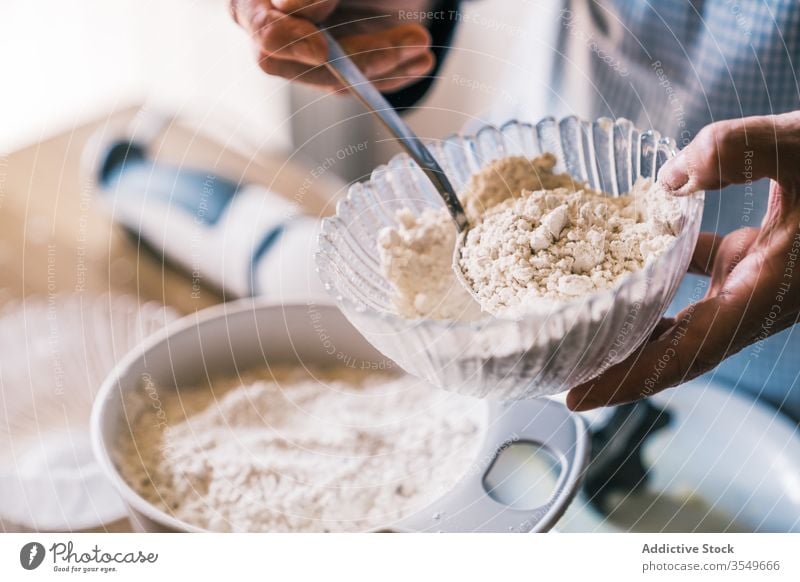 Crop senior cook pouring flour into bowl in kitchen dough add confectioner prepare muffin apron glass spoon pastry process elderly make ingredient bakery aged