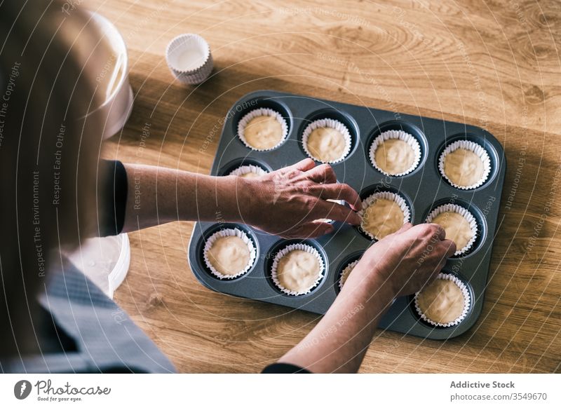 Senior housewife preparing dough in muffin cases pour fill tray batter kitchen senior female home confectioner cook prepare paper liner muffin liner
