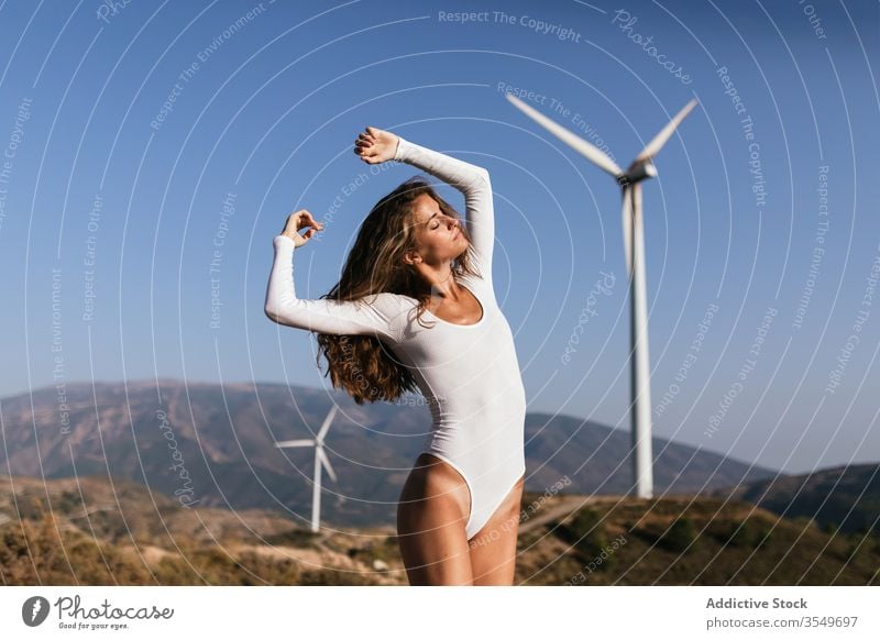 Tender female dancing alone near wind farm on sunny field woman dance countryside sensual nature ecology slim style hand up alternative windmill energy move