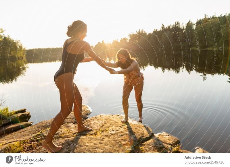 Girlfriends in swimsuits on lake shore at sunset girlfriend holding hands summer vacation together women young relax calm scenery magnificent forest enjoy water