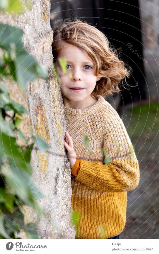 Happy blond child with long hair outside boy childhood tree hide park kid cute white happy portrait little caucasian people young smile happiness fun casual