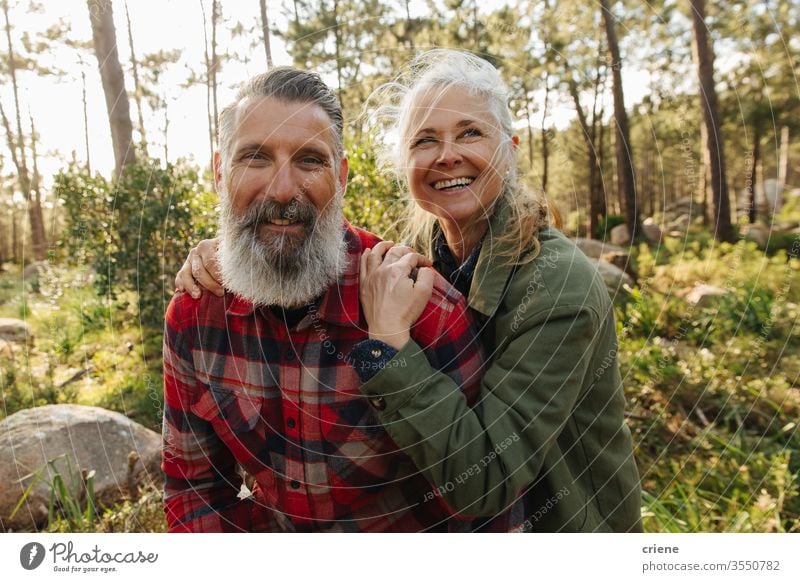 Portrait of happy smiling senior couple on hike in forest portrait looking at camera sunny laughing candid family travelers sports caucasian woods adventure