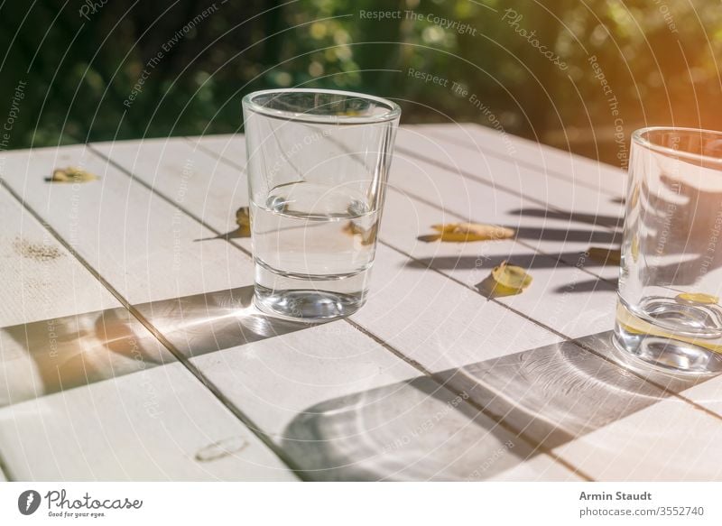 two glasses on a table with autumn leaves aqua background beverage clean clear closeup cool drink empty exterior flare fresh freshness half-full hand light