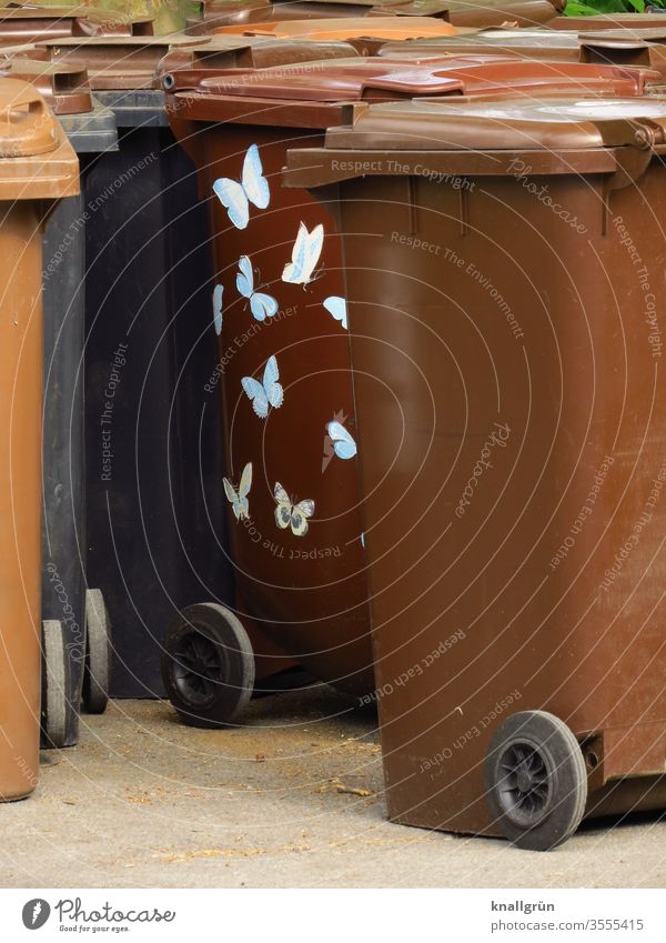 Brown garbage cans, one of them with bright butterfly stickers Waste bins Butterfly Signs and labeling Colour photo Deserted White Day Copy Space right Wheels