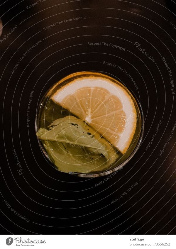 Glass with a leaf and half a slice of lemon from above on a black background drink Drinking vessel Cocktail Longdrink Beverage Alcoholic drinks Colour photo