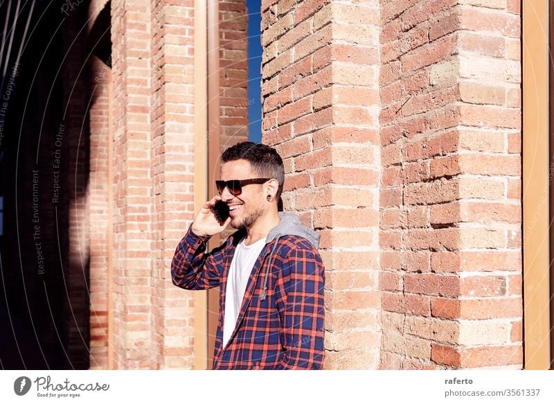 Young bearded man leaning on a bricked wall wearing sunglasses while using a smartphone outdoors. person 1 male communication mobile business businessman call