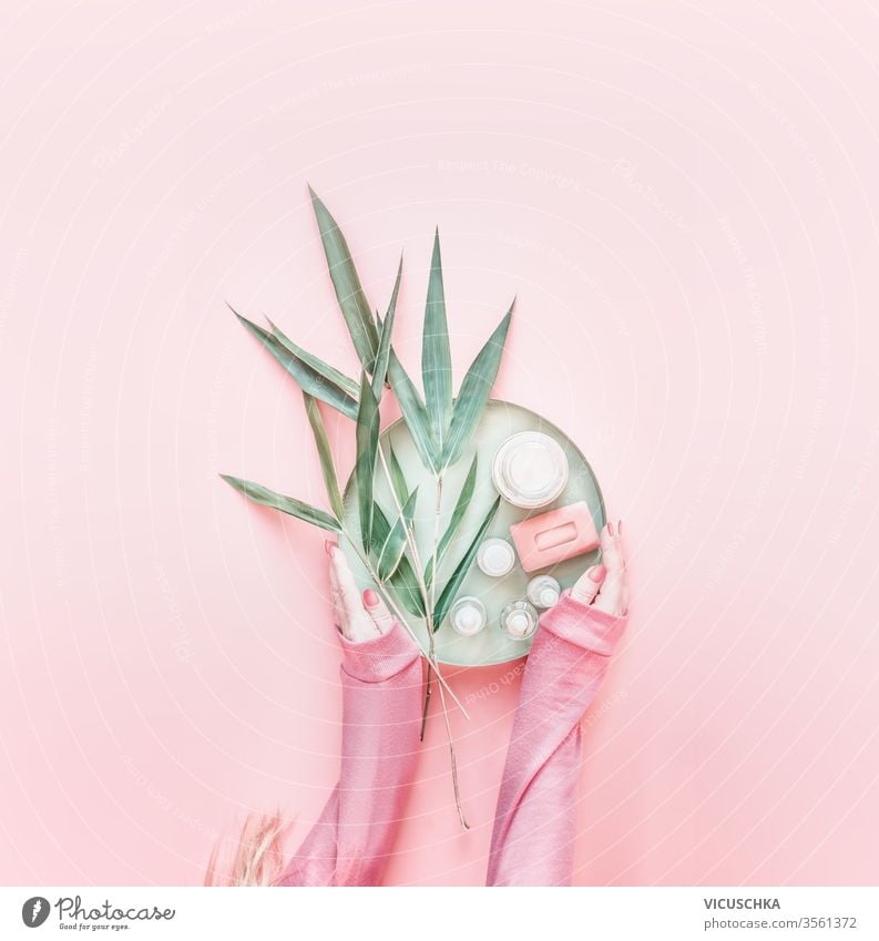 Female hands in pink hoodie holding natural cosmetic products and bamboo leaves on pastel pink background. Modern skin care. Zero waste. Flat lay.  Beauty blog layout. Top view
