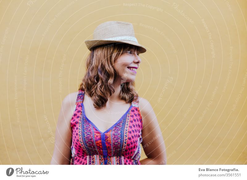 portrait of young caucasian woman outdoors over yellow background. summer time city happy lifestyle curvy real people real life urban hat modern smiling trendy