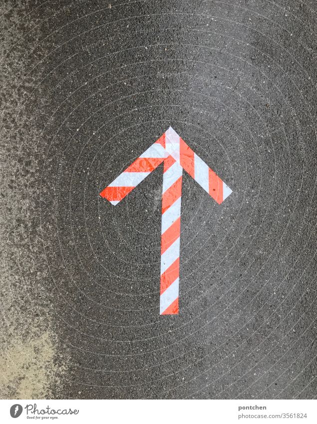 Orientation. An arrow of red-white adhesive tape shows the way on wet asphalt Arrow Road marking Reddish white Adhesive tape Direction Signs and labeling