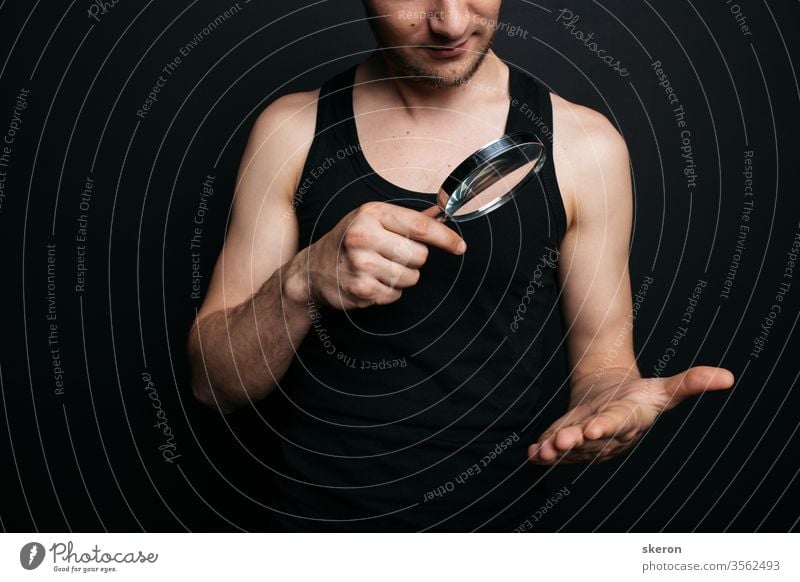 curious guy with a short haircut and a small beard looks at the world around him and the situation through a magnifying glass. concept: dermatological diseases. male with heterochromia of the eye