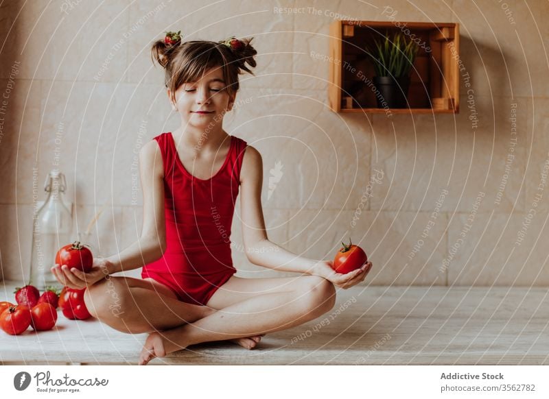 Little girl meditating with tomatoes meditate kitchen concept lotus pose yoga healthy red bright cute barefoot bodysuit home sit counter lifestyle calm peaceful