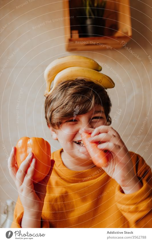Happy teenager playing with fruits and vegetables kitchen preteen concept home overweight smile diet food healthy boy pepper carrot banana male chubby child kid
