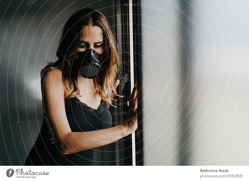 Young woman in respirator mask standing near glass wall isolation covid coronavirus concept prevent lock selective focus protect confine sad stress suffer