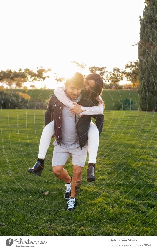 Happy couple having fun on green meadow piggyback together happy love field grass relationship park positive cheerful young nature bonding smile wife carefree
