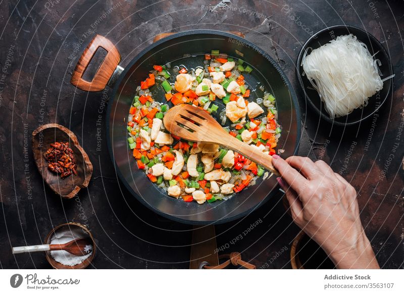 Woman cooking ingredients for noodle dish prepare pan mix stir food chicken vegetable fry hand woman process spatula oriental cuisine natural aromatic tradition