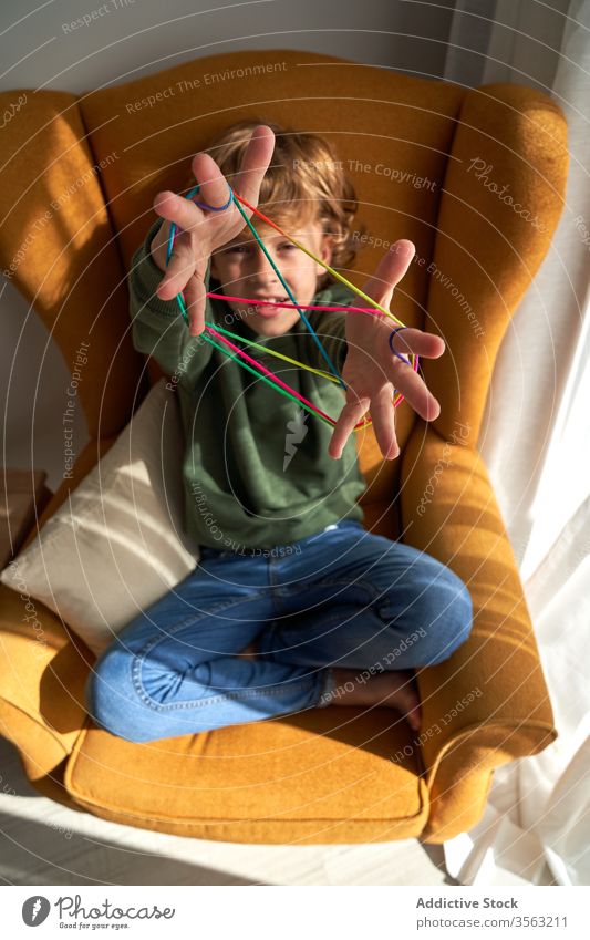 Happy boy enjoying string game at home kid play cat cradle creative chair cheerful cozy happy rest trick brainteaser puzzle focus entertainment sit positive