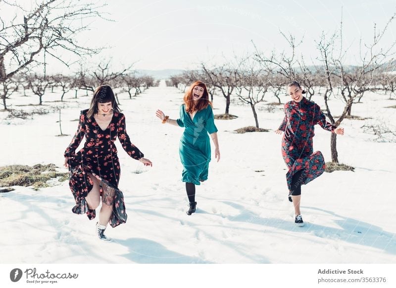Happy fashionable women running on snow together happy fun winter field friend cheerful trendy nature style female young joy smile relax relationship laugh